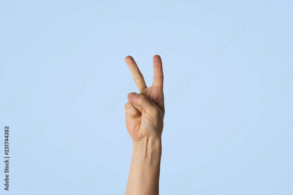 Male hand with two fingers raised against a blue background. Side picture. Peace gesture, greeting Male hand with two fingers raised against a blue background. Side picture. Peace gesture, greeting