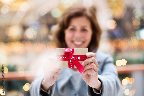 A senior woman with a present in shopping center at Christmas time.