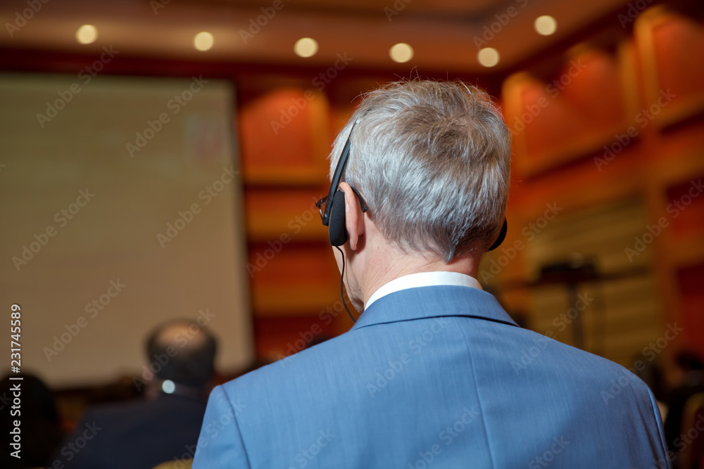 Unrecognizable business people using headphones for translation during event . bald security guard with the headset to control people . heated debate at a conference discussion Unrecognizable business people using headphones for translation during event . bald security guard with the headset to control people . heated debate at a conference discussion