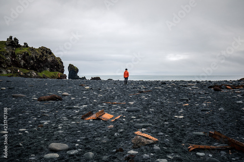 Lonely person in bright jacket standing at the Djupalonssandur black beach in Iceland photo