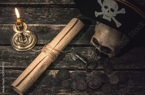Pirate treasure map scroll, pirate captain hat, human skull, ancient coins and burning candle. Treasure hunter concept background.