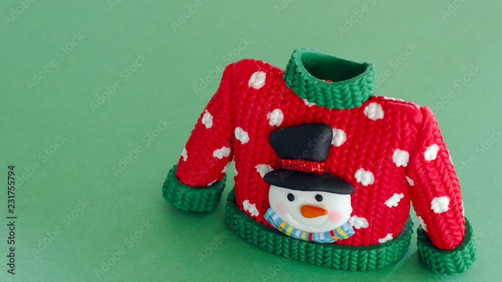 red sweater with green collar and sleeve cuffs white snowflakes and snowman with black hat and carrot nose isolated on festive green background with writing space
