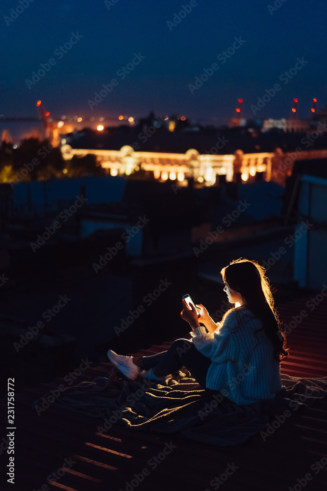 Young girl sits at night on the roof of a house. Beautiful evening Young girl sits at night on the roof of a house. Beautiful evening
