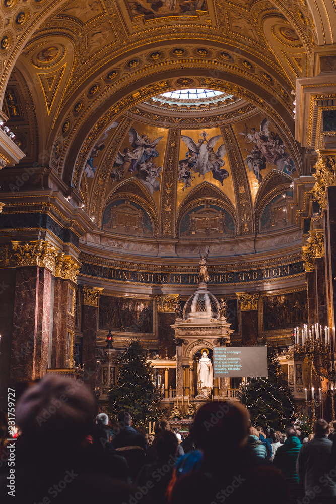 Obraz premium The interior of the main Basilica of Hungary, a large Christmas tree inside the church and many people came to pray at the Christmas. Many gold decorations and icons.