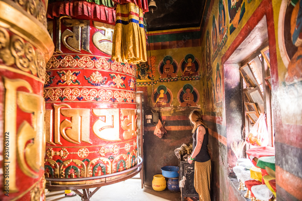 Fototapeta premium A woman stands next to a large prayer wheel of the temple of Boudhanath Stupa, Kathmandu, Nepal, Asia