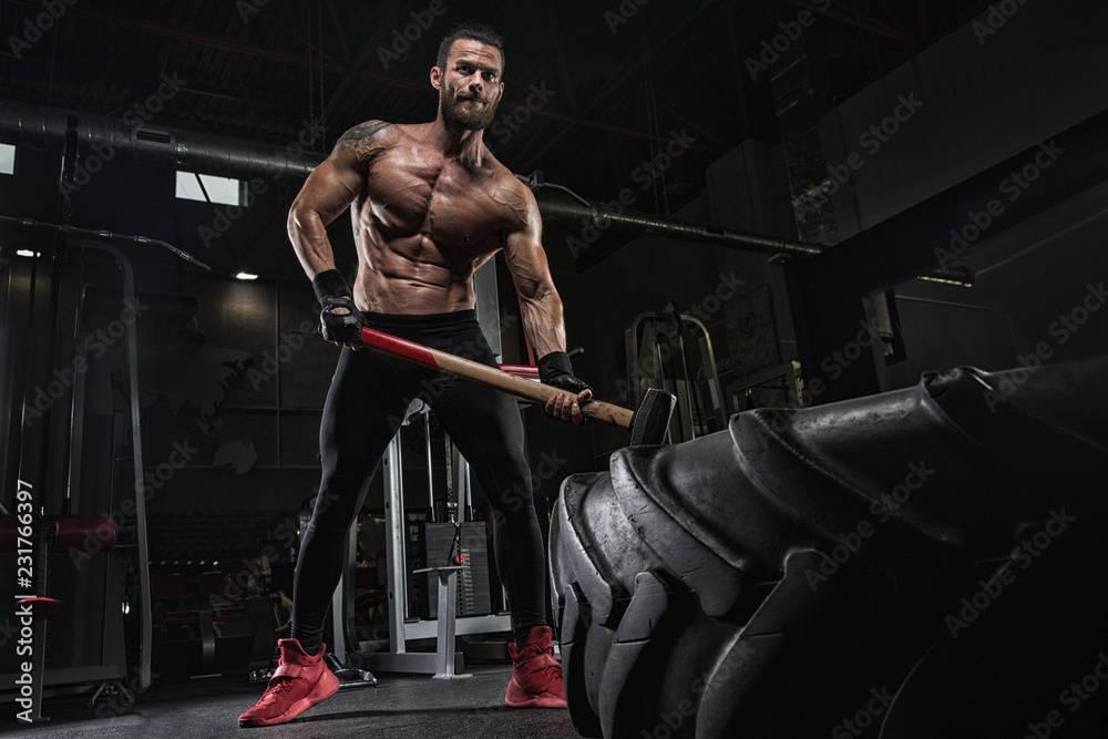Young handsome athlete bodybuilder, weightlifter, doing crossfit, with a sledgehammer, in a modern gym. Concept-strength, beauty, power, sport, health, sports nutrition, diet, styroydy, scales. Young handsome athlete bodybuilder, weightlifter, doing crossfit, with a sledgehammer, in a modern gym. Concept-strength, beauty, power, sport, health, sports nutrition, diet, styroydy, scales.