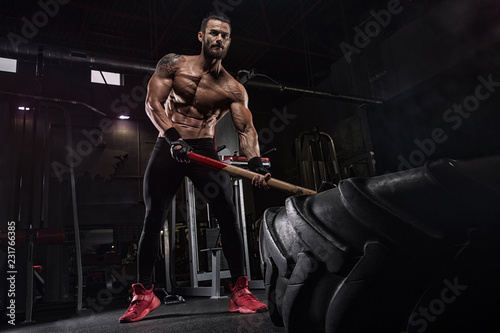 Young handsome athlete bodybuilder, weightlifter, doing crossfit, with a sledgehammer, in a modern gym. Concept-strength, beauty, power, sport, health, sports nutrition, diet, styroydy, scales.