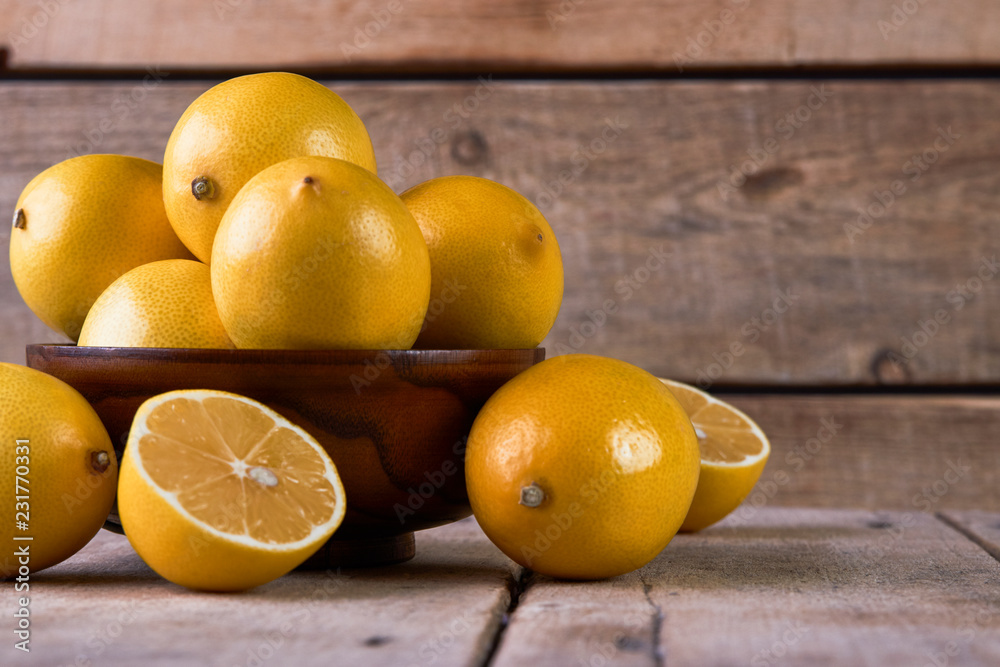 Fresh lemons in a wooden bowl on wood background with copy space