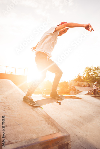 Male teenager performing skateboard tricks against golden sunset photo
