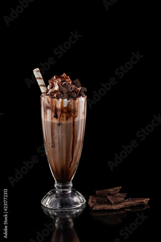 Closeup glass of chocolate milkshake decorated with caramel and whipped cream isolated at black background.