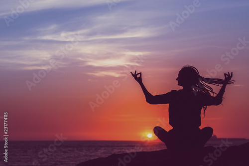 Yoga silhouette. Young woman meditation on the ocean during surrealistic sunset.