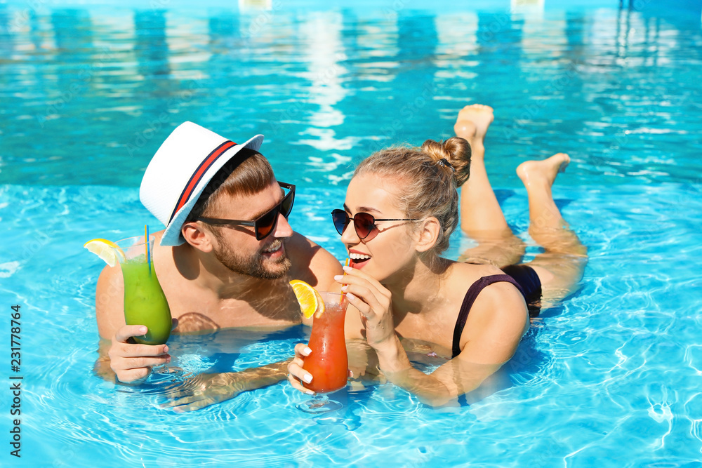 Obraz premium Young couple with refreshing cocktails in swimming pool at resort