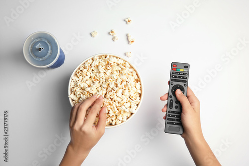 Woman with TV remote eating popcorn on white background, top view. Watching cinema