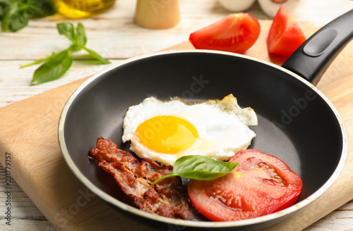 Pan with fried sunny side up egg, bacon and tomato on table