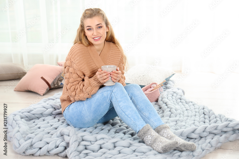 Attractive young woman in cozy warm sweater with cup of hot drink sitting on floor at home Attractive young woman in cozy warm sweater with cup of hot drink sitting on floor at home