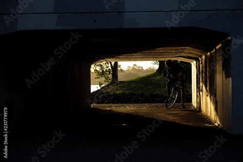 A silhouette of a man on a bike at the other end of a tunnel during golden house photo