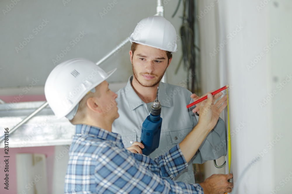 builder and appentice measuring wall with tape measure builder and appentice measuring wall with tape measure