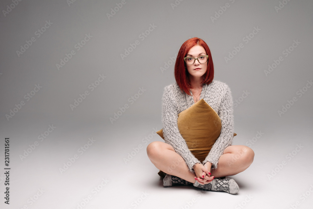 Red haired girl in grey sweater and warm socks sitting on floor in Turkish  style and
