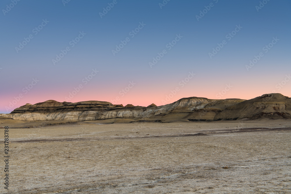 The desert landscape and hills of the Bisti Badlands of New Mexico at sunset under a beautiful sky with pink, peach, purple, and blue hues
