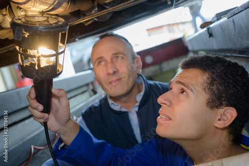 mechanics using torch to look under car at repair garage