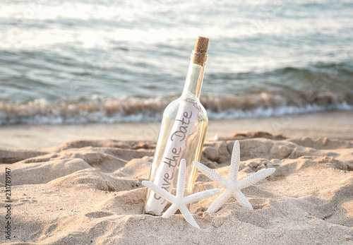 white starfish couple in beach sand with save the date message in a bottle