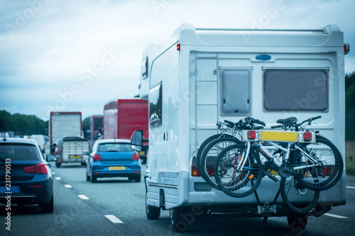 Closeup of busy Highway transportation  motorway full of cars in the evening with dark cloudy blue sky and one Caravan carrying bikes