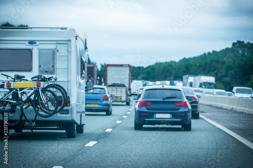 Closeup of busy Highway transportation motorway full of cars in the evening with dark cloudy blue sky and one Caravan carrying bikes