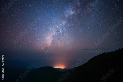 Milky way above the mountains peak with light from the village and noise