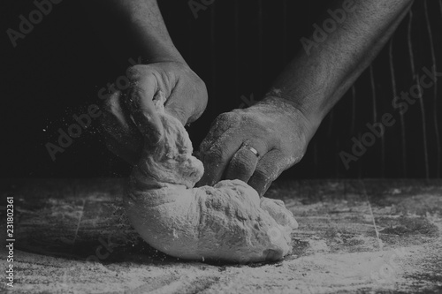 Man with apron kneading a ball of dough on wooden board by hand in artistic conversion