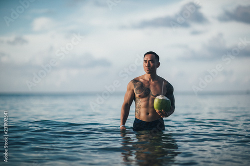 Tattooed Muscular  Guy Holding Coconut in Ocean