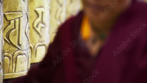 Unrecognizable buddhist monk touching and rotating metal prayer wheels in Macleod Ganj residence of Dalai Lama