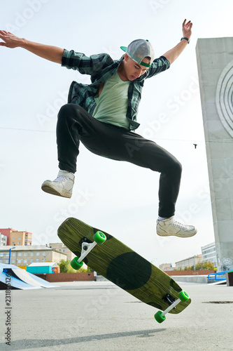 Full length portrait of contemporary young man doing skateboard stunts outdoors in extreme park