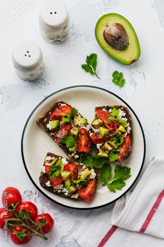 Avocados, cherry tomatoes and feta cheese sandwiches with balsamic sauce and cilantro on old olive board. Top view.