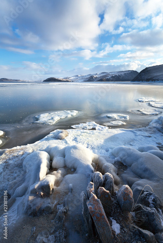 Lake Baikal in December. Beautiful winter landscape with thin ice in the Strait of Olkhon Gate and the ice-covered shore on a sunny frosty day