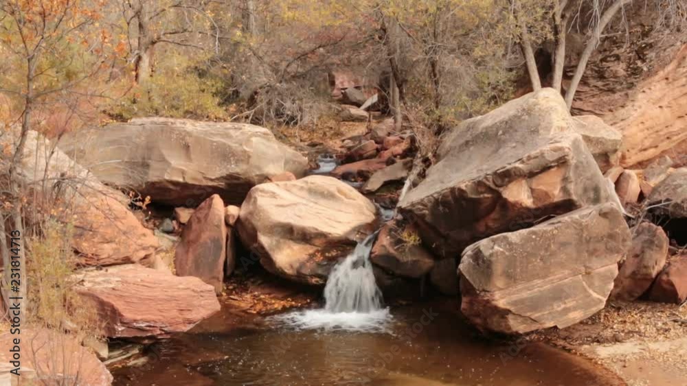 A small waterfall on the Left Fork (Subway) in Zion National park pours over sandstone boulders while golden autumn leaves drift down from the trees as a breeze stirs the branches. A small waterfall on the Left Fork (Subway) in Zion National park pours over sandstone boulders while golden autumn leaves drift down from the trees as a breeze stirs the branches.