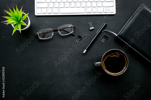 Black strict office desk, monochrome. Computer keyboard, expensive black notebook, glasses, coffee. Top view copy space