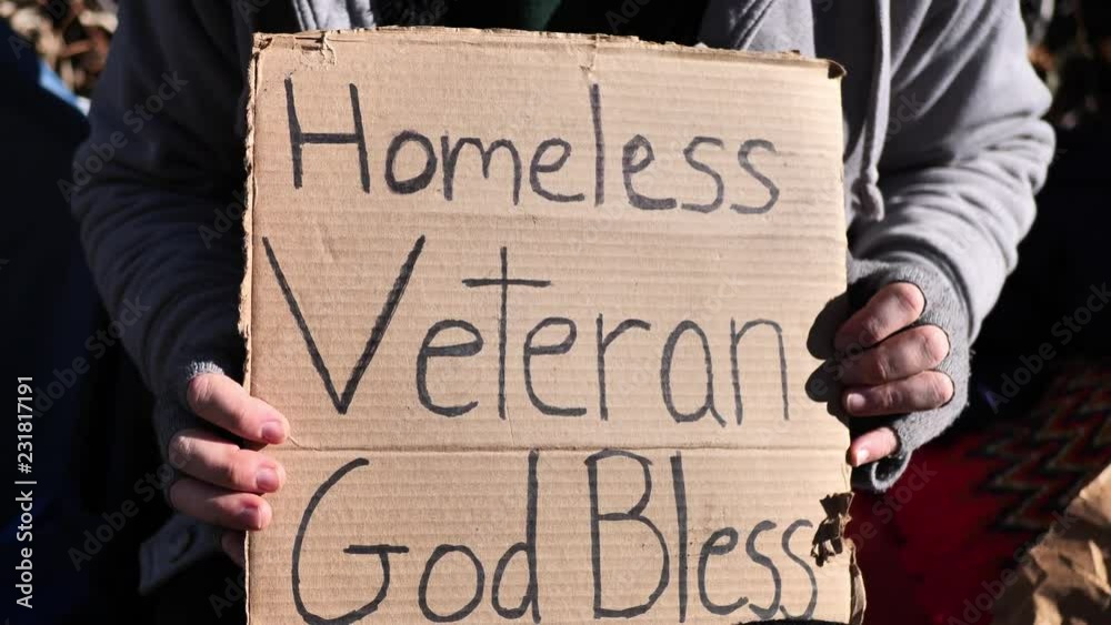 Homeless veteran sitting and holding cardboard sign, talking with his hands, interview styled.
