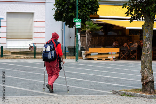 A woman with crutches and a backpack goes along the sidewalk. View from the back.