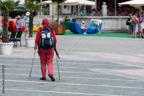 A woman with crutches and a backpack goes along the sidewalk. View from the back.