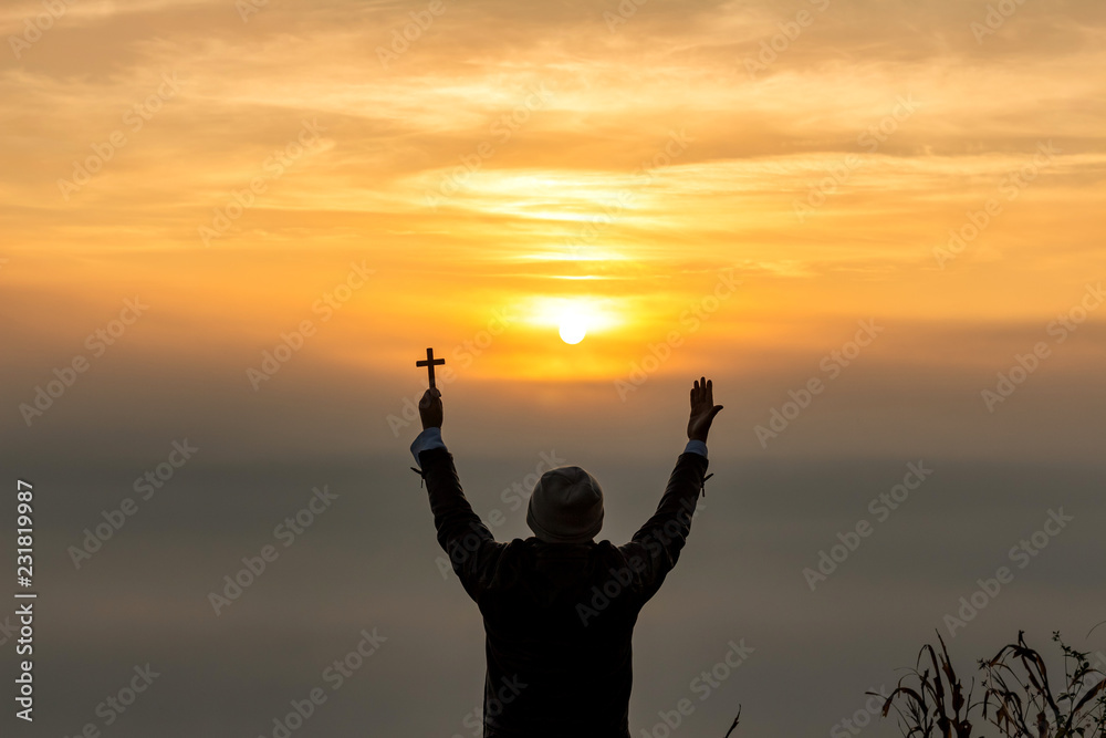 human praying to the GOD while holding a crucifix symbol with bright sunbeam on the sky at morning misty landscape