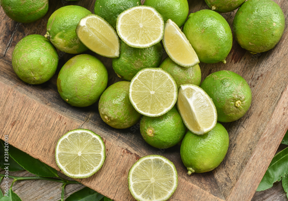 Fresh green lime with some slices and cut pieces on wooden tray background. Fresh green lime with some slices and cut pieces on wooden tray background.