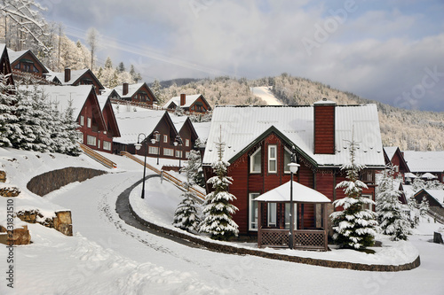 Traditional wooden houses on a hill slope in the mountains of Carpathians surrounded by snow-capped fir trees.