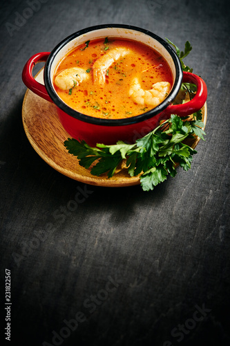 traditional Thai soup with shrimp and coconut milk in a red pot with parsley