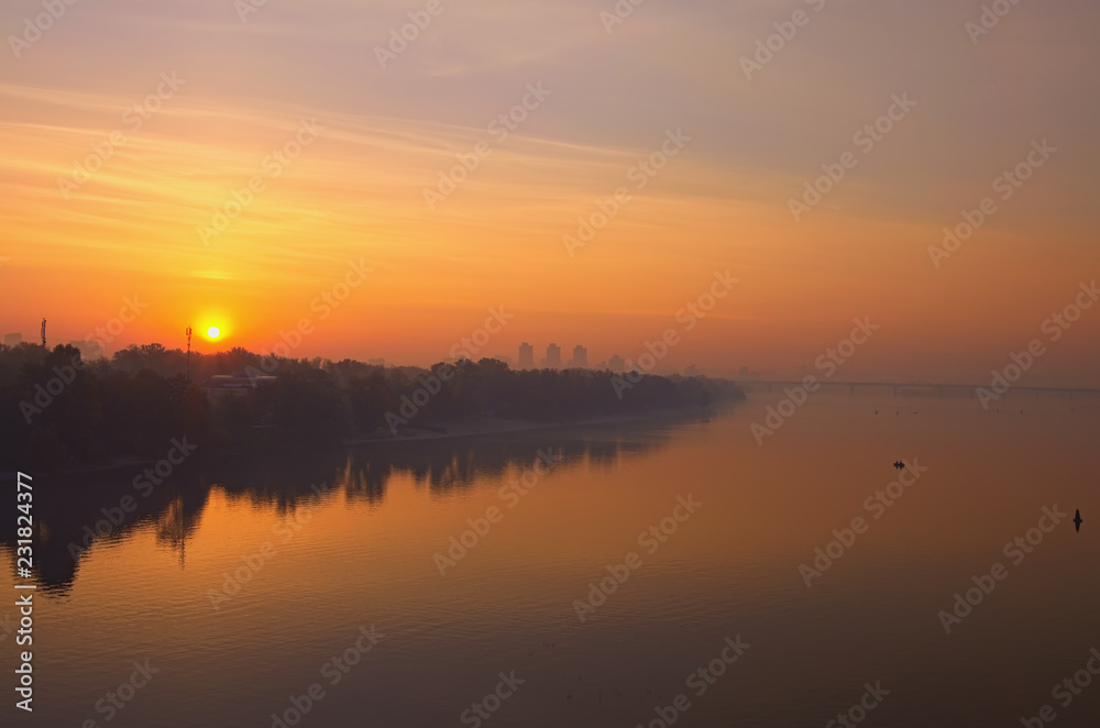Landscape panorama of Dnipro River. Magnificent autumn sunrise in Kyiv. Foggy morning landscape. Beautiful city view with rising sun and fiery sky. Kyiv (Kiev), Ukraine