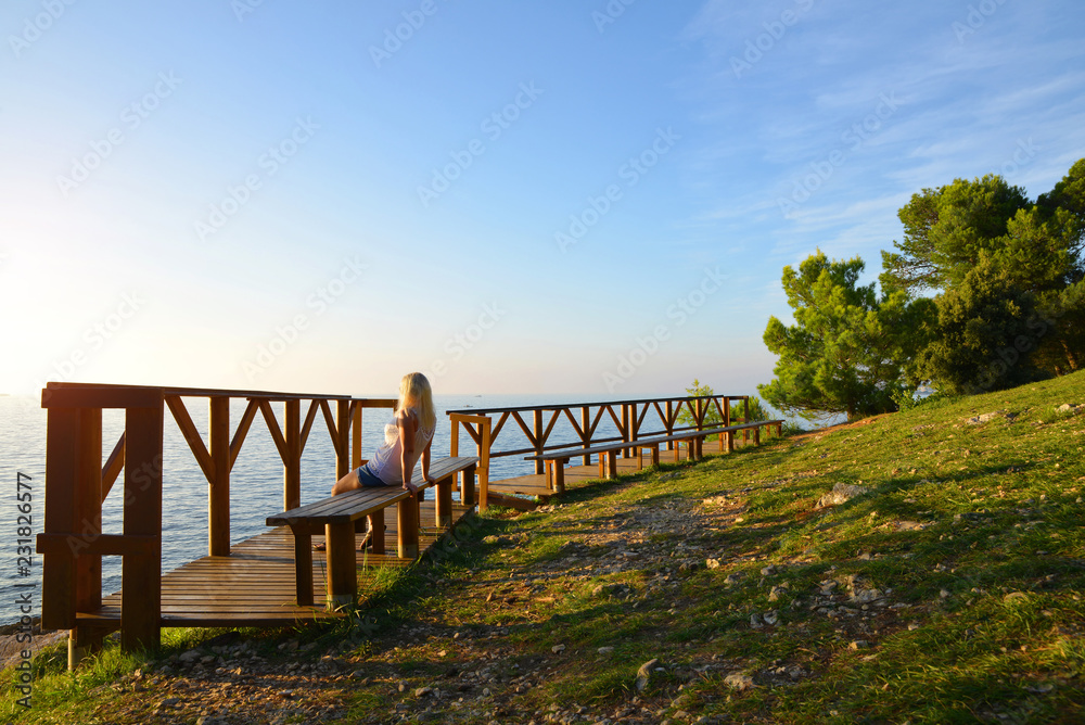 Obraz premium A woman sitting on a bench is watching the sunset over the sea.