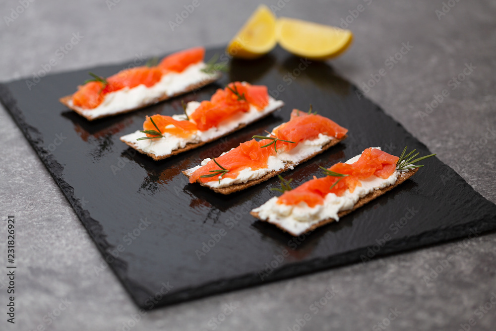 Tasty snack with salmon and soft cheese on a black plate Tasty snack with salmon and soft cheese on a black plate