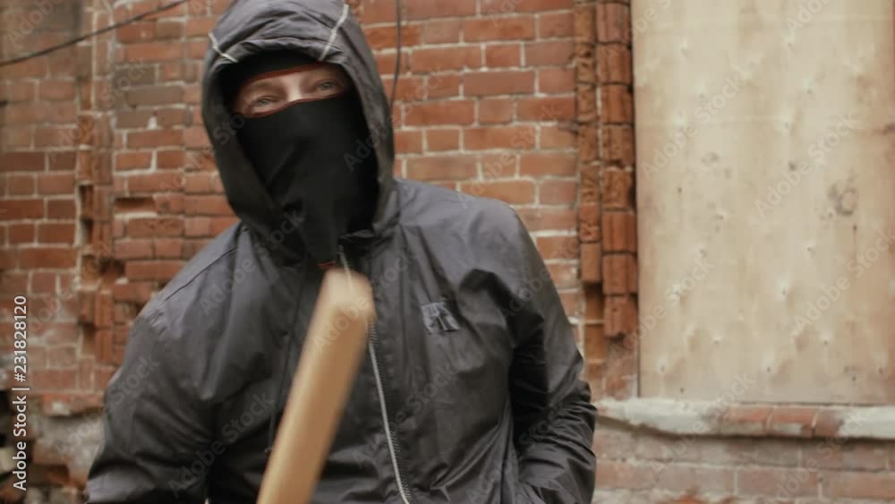 Aggressive hooligan in mask threatening to camera with baseball bat Aggressive hooligan in mask threatening to camera with baseball bat