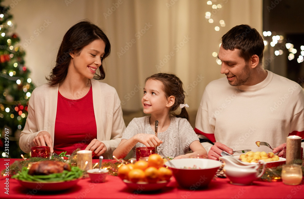 holidays, family and celebration concept - happy mother, father and little daughter having christmas dinner at home holidays, family and celebration concept - happy mother, father and little daughter having christmas dinner at home