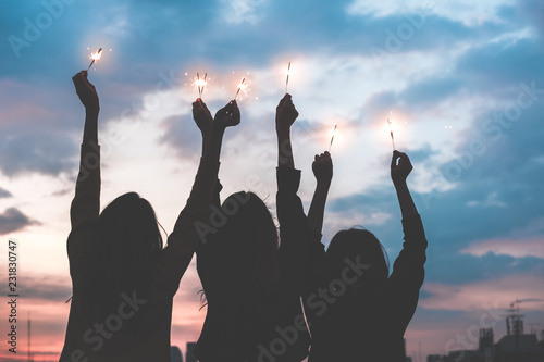 silhouette happy group of asia girl friends enjoy and play sparkler at rooftop party at evening sunset,Holiday celebration festive,teeage lifestyle,freedom and fun. photo