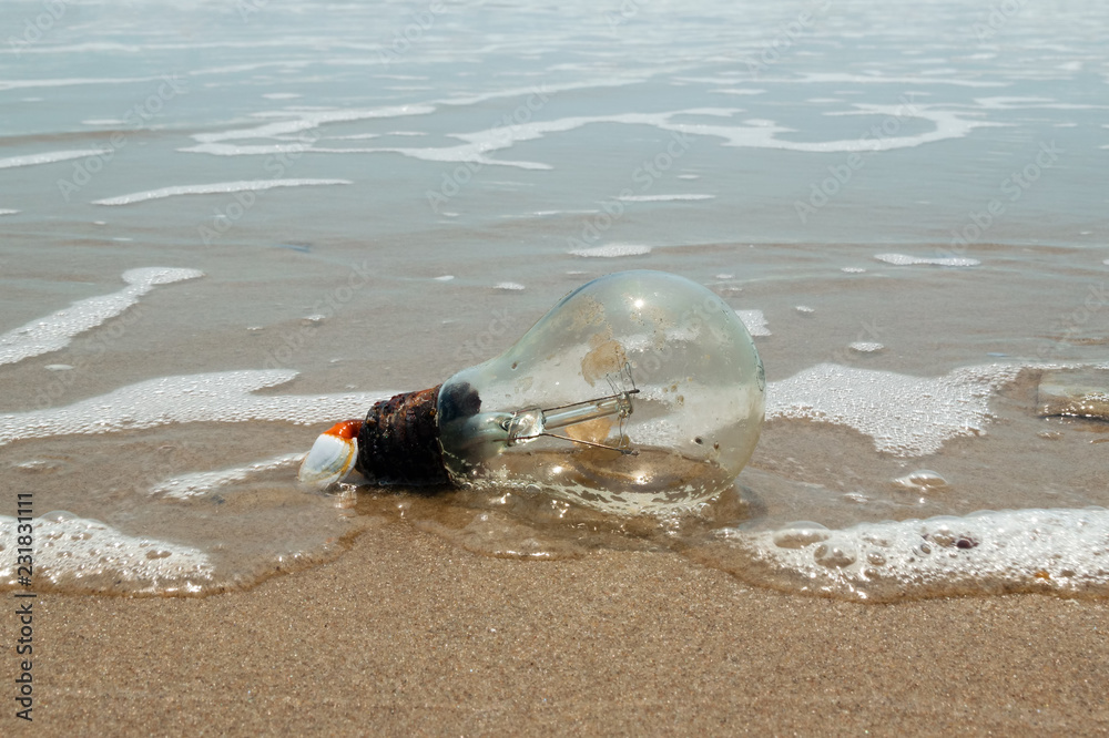 Obraz premium Old light bulb on a sandy beach near to the sea. Pollution of a coastline. Vung Tau, Vietnam.